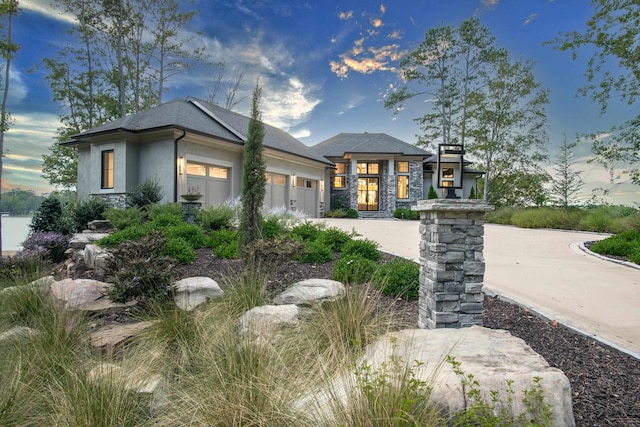 prairie-style home with a garage, stone siding, driveway, and stucco siding