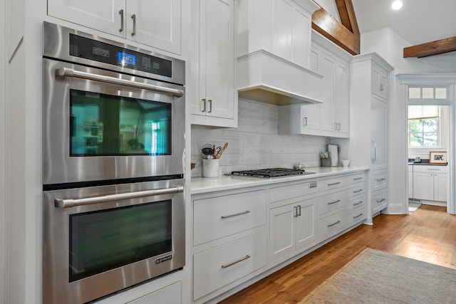 kitchen with lofted ceiling, appliances with stainless steel finishes, white cabinetry, light hardwood / wood-style floors, and decorative backsplash