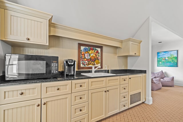 kitchen with sink, dark stone counters, crown molding, cream cabinets, and light carpet