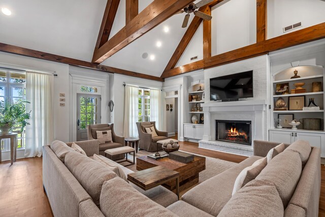 living room featuring light hardwood / wood-style flooring, built in shelves, a fireplace, and beamed ceiling