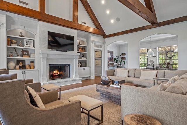 living room featuring built in shelves, beam ceiling, high vaulted ceiling, hardwood / wood-style flooring, and a fireplace