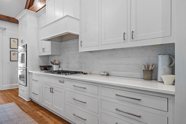 kitchen with premium range hood, appliances with stainless steel finishes, backsplash, light hardwood / wood-style floors, and white cabinets