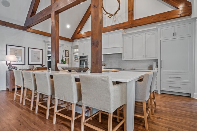 kitchen featuring a spacious island, a breakfast bar area, white cabinetry, stainless steel oven, and decorative backsplash