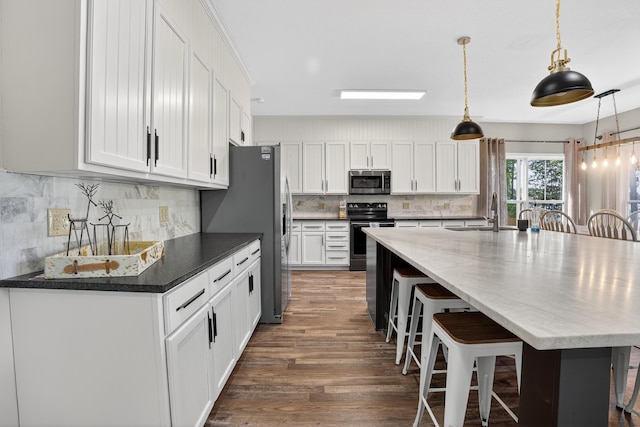 1005 Dennis St, Eatonton, GA 31024 - kitchen with appliances with stainless steel finishes, a kitchen bar, white cabinets, wood finished floors, and tasteful backsplash