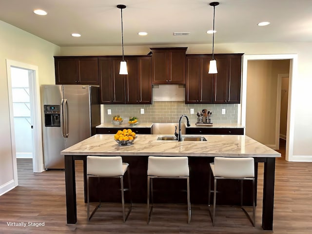 kitchen featuring a center island with sink, a breakfast bar area, hanging light fixtures, stainless steel refrigerator with ice dispenser, and a sink