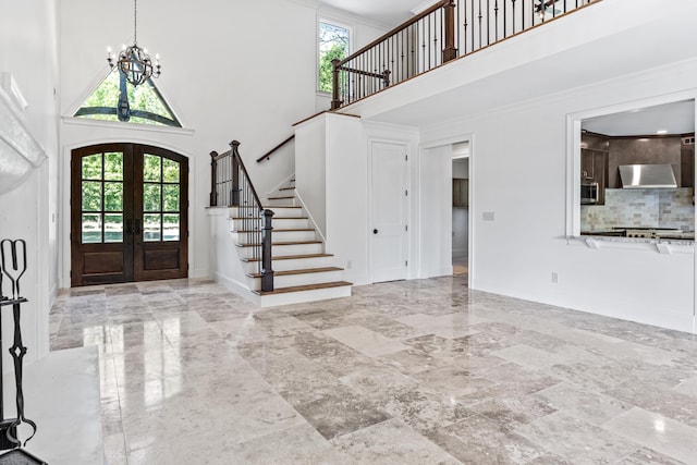 entryway featuring a high ceiling, ornamental molding, a chandelier, and french doors