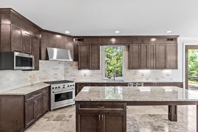 kitchen with sink, dark brown cabinets, appliances with stainless steel finishes, a kitchen island, and light stone countertops