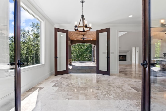 entrance foyer with a notable chandelier, crown molding, a fireplace, and french doors