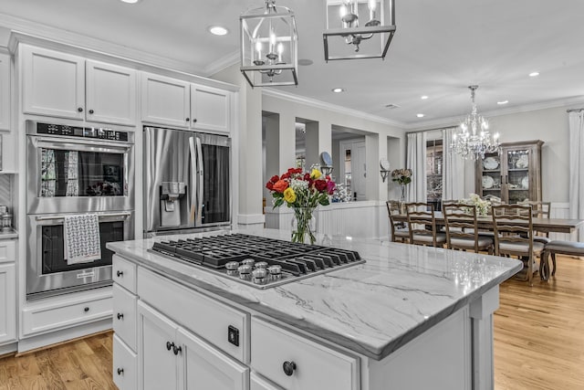 kitchen with appliances with stainless steel finishes, a kitchen island, light wood-style flooring, and ornamental molding