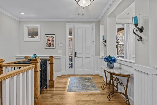 foyer entrance featuring ornamental molding, a wainscoted wall, visible vents, and light wood-style floors