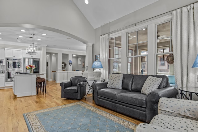 living area with arched walkways, ornate columns, crown molding, light wood-style floors, and high vaulted ceiling