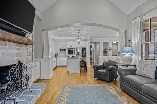 living room with light wood-style floors, crown molding, decorative columns, and a stone fireplace