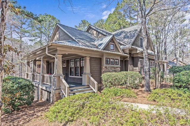 view of front facade featuring covered porch, stone siding, and roof with shingles