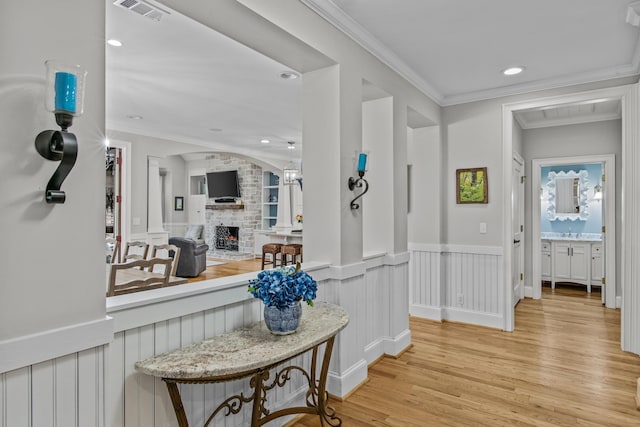 corridor with a wainscoted wall, light wood-style flooring, visible vents, and ornamental molding