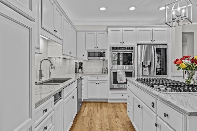 kitchen featuring appliances with stainless steel finishes, a sink, light wood-style floors, white cabinetry, and backsplash