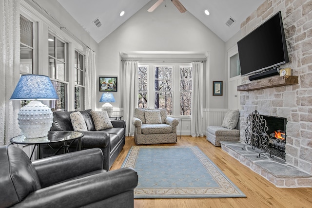 living room featuring visible vents, a wainscoted wall, wood finished floors, a stone fireplace, and high vaulted ceiling