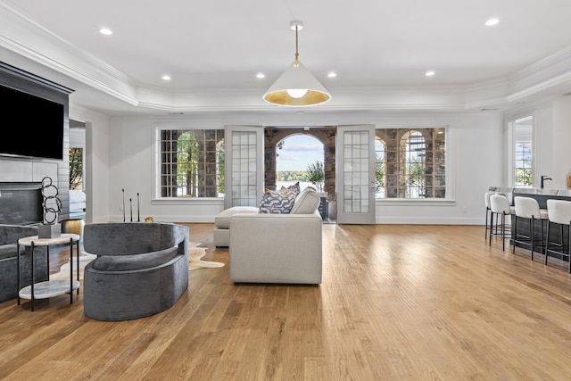 living room featuring a tray ceiling, light hardwood / wood-style flooring, a tile fireplace, and ornamental molding