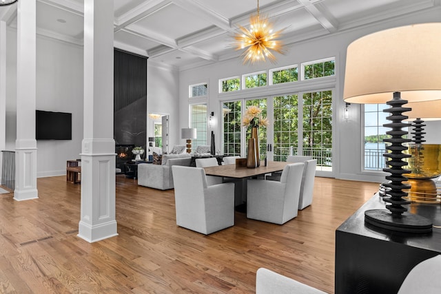 dining room featuring coffered ceiling, an inviting chandelier, a towering ceiling, hardwood / wood-style flooring, and ornate columns