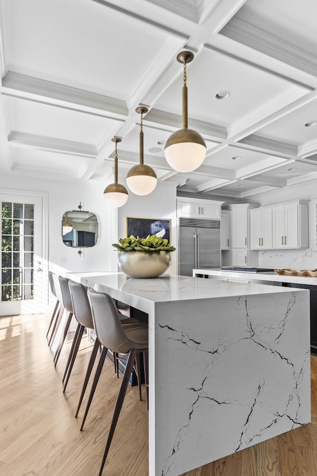 kitchen featuring a large island, light stone counters, pendant lighting, built in fridge, and white cabinetry