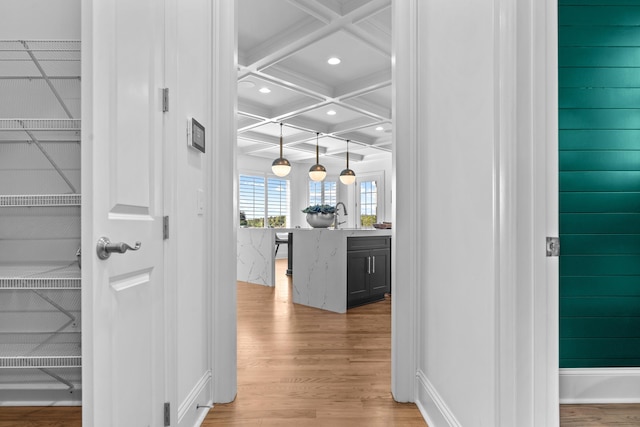 hallway with coffered ceiling, sink, light wood-type flooring, and beam ceiling