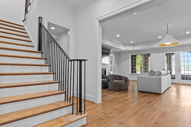 staircase featuring hardwood / wood-style flooring, a large fireplace, crown molding, and french doors