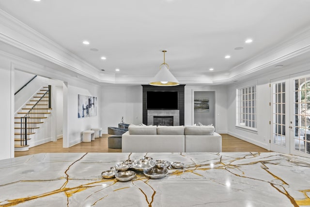 living room with a large fireplace, crown molding, light wood-type flooring, and a raised ceiling