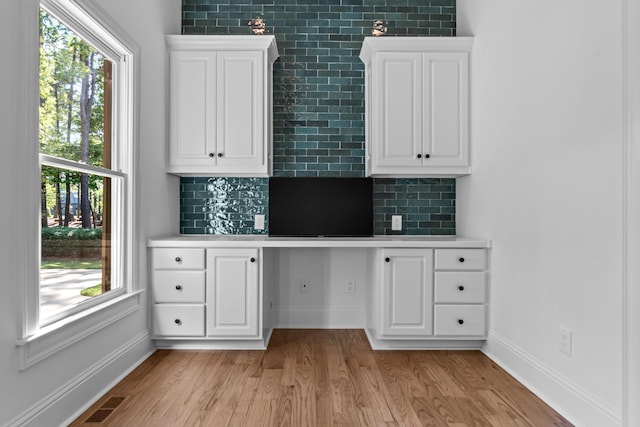 interior space with white cabinets, light hardwood / wood-style floors, built in desk, and backsplash