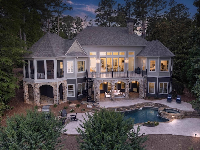 back house at dusk with a patio, a swimming pool with hot tub, a balcony, and an outdoor living space with a fire pit