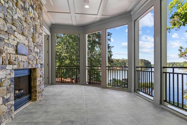 unfurnished sunroom featuring coffered ceiling, plenty of natural light, a water view, and a stone fireplace