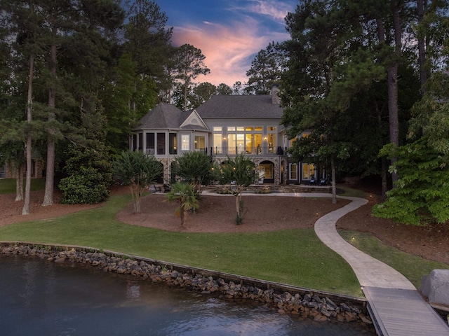 back house at dusk with a yard, a sunroom, and a water view