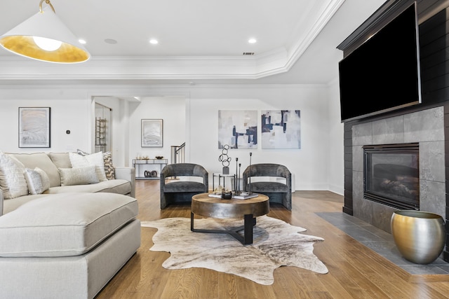 living room featuring a tile fireplace, a tray ceiling, wood-type flooring, and ornamental molding