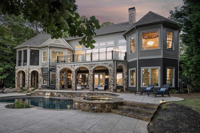 back house at dusk with a sunroom, a patio area, a balcony, and a swimming pool with hot tub