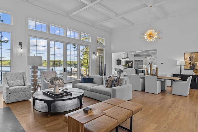 living room featuring light wood-type flooring, a high ceiling, an inviting chandelier, and coffered ceiling