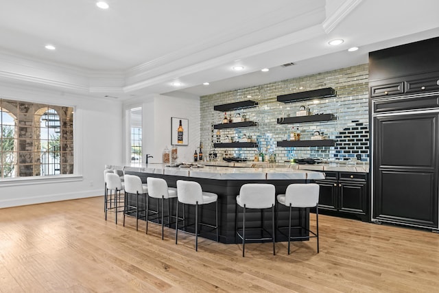 bar featuring light wood-type flooring, light stone countertops, a tray ceiling, ornamental molding, and paneled built in fridge