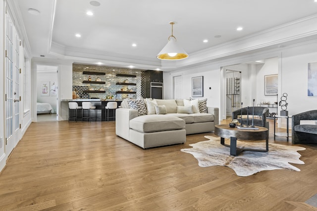 living room with light wood-type flooring, crown molding, and a raised ceiling