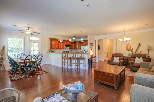 living room featuring decorative columns, crown molding, ceiling fan with notable chandelier, and dark hardwood / wood-style flooring