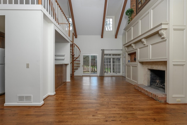 unfurnished living room with visible vents, stairway, dark wood-type flooring, a fireplace, and high vaulted ceiling