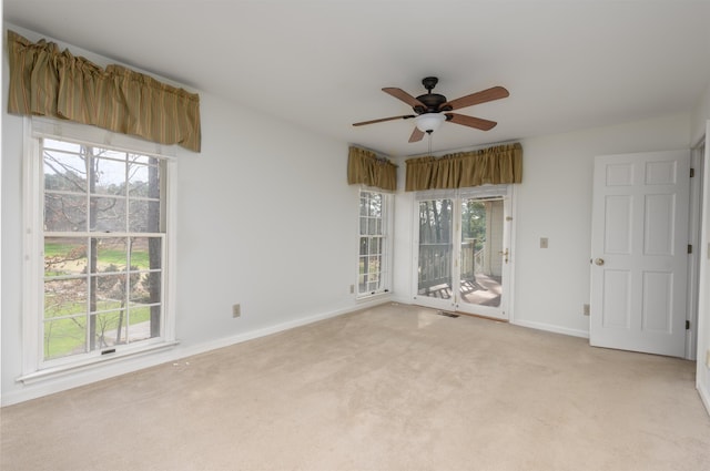 empty room featuring a healthy amount of sunlight, light carpet, ceiling fan, and baseboards