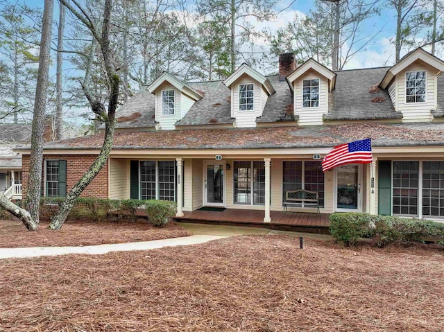 view of front of home featuring a porch, brick siding, a chimney, and roof with shingles