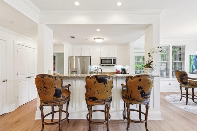 1010A Creekside, Greensboro, GA 30642 - kitchen featuring appliances with stainless steel finishes, light stone countertops, a breakfast bar area, light wood-type flooring, and ornamental molding