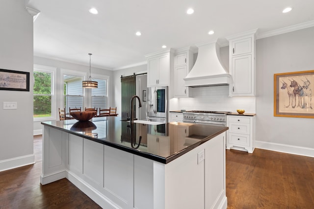 855 Jasper St, Madison, GA 30650 - kitchen with premium range hood, dark countertops, appliances with stainless steel finishes, a barn door, and dark wood finished floors