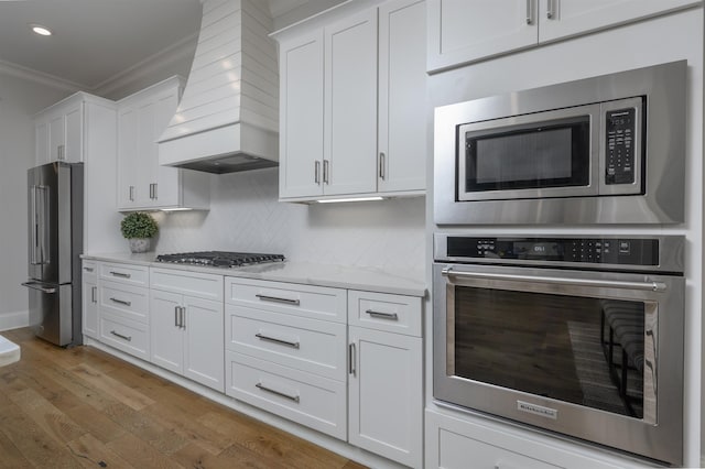 kitchen with wood finished floors, stainless steel appliances, crown molding, light countertops, and custom exhaust hood