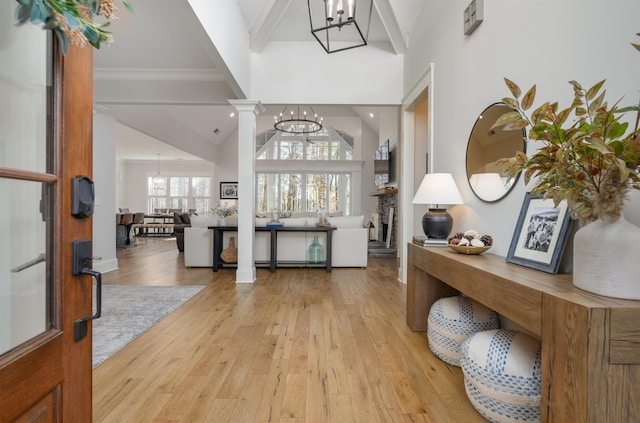 foyer featuring ornate columns, beamed ceiling, an inviting chandelier, and light wood finished floors