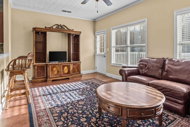 living room featuring crown molding, ceiling fan, light hardwood / wood-style floors, and a textured ceiling