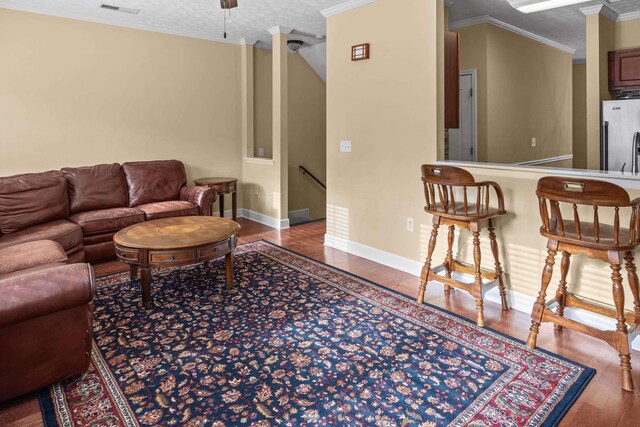 living room with wood-type flooring, ornamental molding, and a textured ceiling