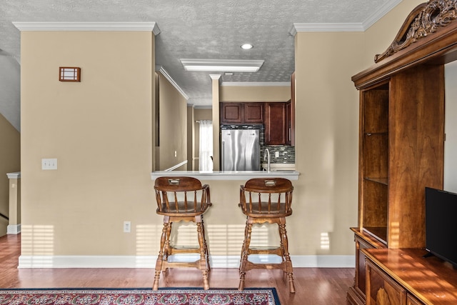 kitchen featuring a breakfast bar, stainless steel refrigerator, ornamental molding, dark hardwood / wood-style flooring, and decorative backsplash