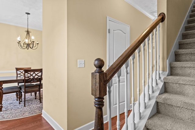 staircase with a notable chandelier, wood-type flooring, and ornamental molding