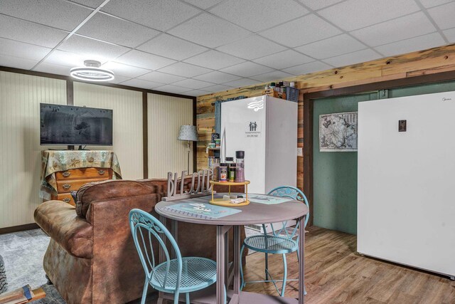 dining area featuring wood-type flooring, wooden walls, and a paneled ceiling