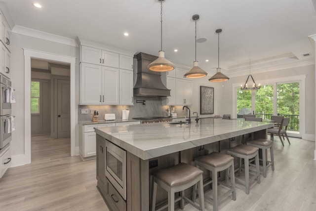 kitchen featuring custom exhaust hood, white cabinetry, hanging light fixtures, a large island, and light stone countertops