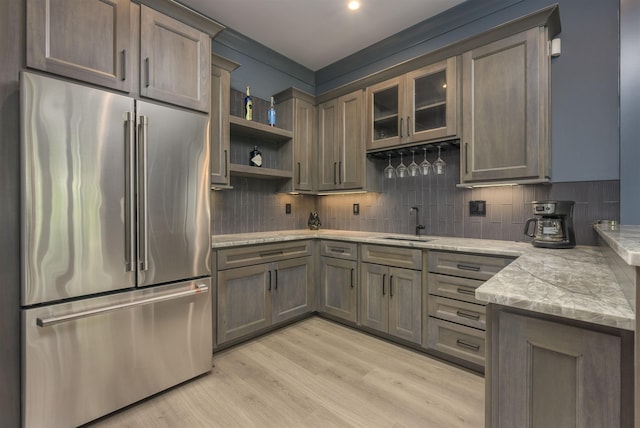 kitchen with high end fridge, sink, light stone counters, light wood-type flooring, and backsplash